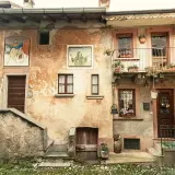 Antica facciata con affreschi e balcone fiorito. Un invito a scoprire cosa vedere ad Arcumeggia, tra arte e storia.