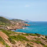 Costa selvaggia tra Alghero e Bosa, con macchia mediterranea, rocce dorate e mare turchese.