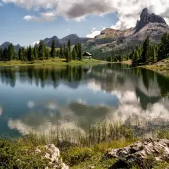 Lago alpino con riflessi di montagne e nuvole, un piccolo rifugio tra i pini. Uno dei paesi più belli del Cadore.