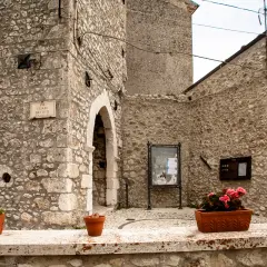 Un angolo suggestivo di Castel del Monte, Abruzzo, con muri in pietra grezza, un arco antico e vasi fioriti che aggiungono colore.