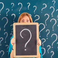 Ragazza con lavagna piena di punti interrogativi, come per le prove invalsi che sono obbligatorie.