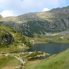 Sentiero panoramico per il giro dei 5 laghi a Madonna di Campiglio, con escursionisti che ammirano il lago alpino e le montagne circostanti.