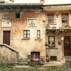Antica facciata con affreschi e balcone fiorito. Un invito a scoprire cosa vedere ad Arcumeggia, tra arte e storia.
