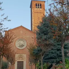 San Celso a Milano, con il suo campanile in mattoni rossi e la facciata ornata da un rosone, circondato da alberi dalle foglie autunnali.