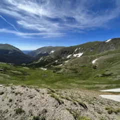Vasta valle alpina con prati verdi, macchie di neve e cielo azzurro. Un paesaggio mozzafiato che ricorda l'altitudine chiusa di Bolzano.