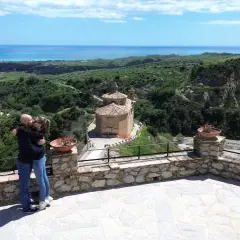 Coppia si bacia con vista panoramica su Badolato, Calabria, con il mare all'orizzonte e una chiesa antica.