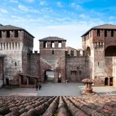Il castello di Soncino, con le sue imponenti torri in mattoni rossi e le mura merlate, si staglia sotto un cielo azzurro e nuvoloso.