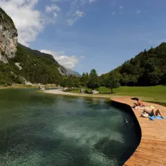 Persone si rilassano sul pontile in legno del lago di Nembia, circondato da montagne verdi e acqua cristallina.