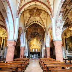 Interno dell'abbazia di Viboldone con volte affrescate, colonne in mattoni e panche di legno.