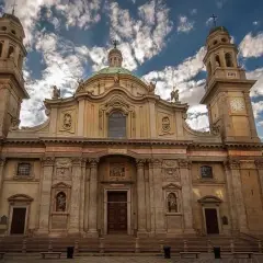 La maestosa facciata della chiesa Sant'Alessandro a Milano, con le sue torri campanarie e la cupola, si staglia contro un cielo azzurro e nuvoloso.