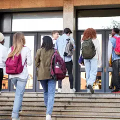 Gruppo di studenti con zaini sale le scale verso l'edificio scolastico, forse per affrontare una grave punizione scolastica.