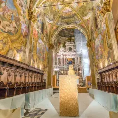 Interno della Certosa di Pavia, con affreschi dorati, stalli lignei e un'impalcatura. Cosa vedere in questo capolavoro.