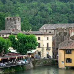 Un pittoresco borghetto sul Mincio con case storiche, torri medievali e un ristorante con tavoli all'aperto affacciato sul fiume.