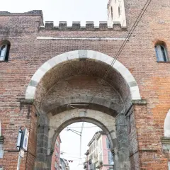 La Porta Ticinese, con i suoi archi in pietra e mattoni rossi, accoglie la vista di una strada milanese.