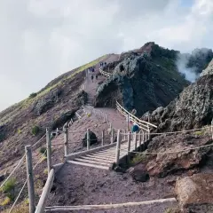 Sentiero sul gran cono Vesuvio, con persone che salgono verso il cratere fumante.
