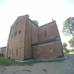 L'imponente facciata in mattoni dell'abbazia di Morimondo si staglia contro il cielo. Alcune persone e biciclette riposano sull'erba.
