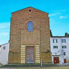 La facciata in pietra grezza di Santa Maria del Carmine domina la piazza, con un grande portale in legno e un rosone blu.