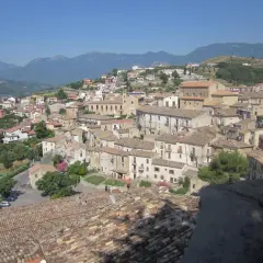 Panoramica di **Altomonte, Calabria**, con tetti in cotto e case arroccate su una collina, sullo sfondo montagne azzurre.