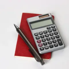 Calcolatrice, penna e taccuino rosso, utili per consultare la tabella importi pensione insegnanti.