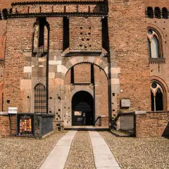 Ingresso principale del castello visconteo di Pavia, con mura in mattoni rossi, finestre ogivali e un ampio portone ad arco.