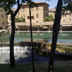 Cascata e portico storico a Bevagna, Umbria. L'acqua scende su gradoni di pietra, riflettendo gli edifici antichi.
