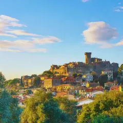 Un caparbio paese arroccato su una collina, con un castello imponente e case colorate, illuminato dalla luce dorata del tramonto.
