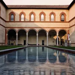 Cortile del Castello Sforzesco con piscina riflettente e portico ad archi.