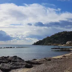 Costa di Pollica con case colorate arroccate sulla collina e mare calmo sotto un cielo nuvoloso.