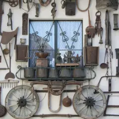 Vecchi attrezzi agricoli e oggetti d'epoca adornano un muro a Bienno, Brescia, creando un'installazione artistica che racconta storie di un tempo passato.