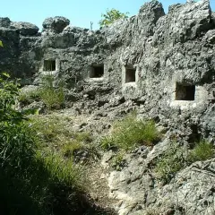 Antiche trincee della Linea Cadorna scavate nella roccia, con feritoie che si affacciano su un paesaggio verdeggiante.