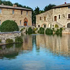 Antiche terme libere a San Gimignano, con edifici in pietra che si specchiano in un laghetto tranquillo.