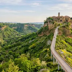 Ponte pedonale verso Civita di Bagnoregio, un borgo medievale arroccato su una rupe, circondato da verdi calanchi.