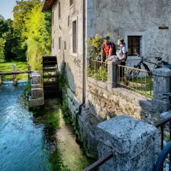 Coppia in bicicletta ammira un antico mulino ad acqua, uno dei tanti borghi friulani da visitare, immersi nel verde e lungo un ruscello cristallino.