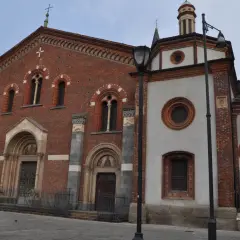 Facciata in mattoni rossi e parte in intonaco bianco della Basilica di Sant'Eustorgio a Milano, con portali decorati e finestre ad arco.