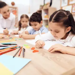 Bambini concentrati scrivono, un'insegnante li osserva. Un'immagine che ispira per una domanda motivazionale TFA sostegno.