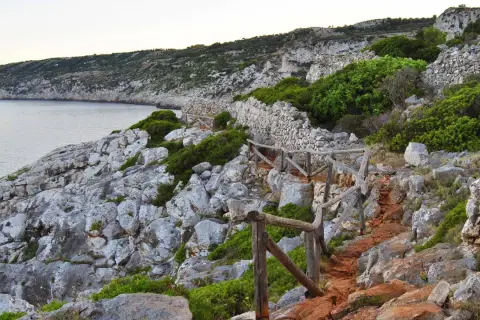 Sentiero roccioso con muretto a secco e vegetazione mediterranea, vicino alle grotte cipolliane.