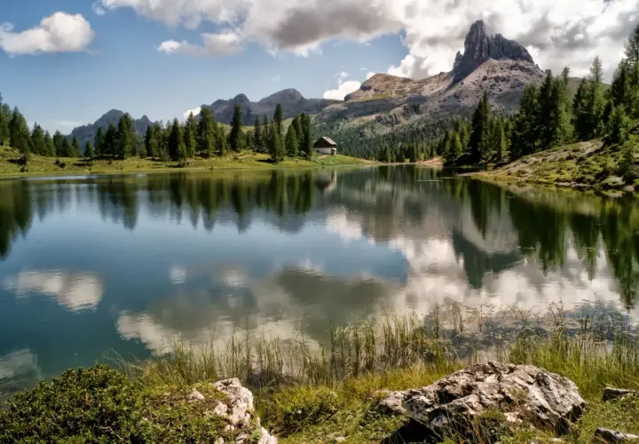 Lago alpino con riflessi di montagne e nuvole, un piccolo rifugio tra i pini. Uno dei paesi più belli del Cadore.