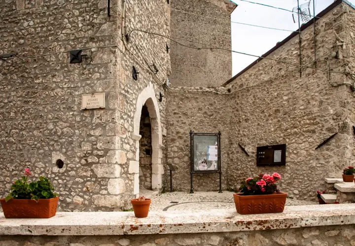 Un angolo suggestivo di Castel del Monte, Abruzzo, con muri in pietra grezza, un arco antico e vasi fioriti che aggiungono colore.