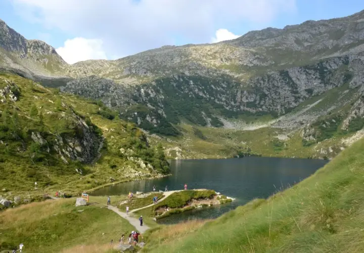 Sentiero panoramico per il giro dei 5 laghi a Madonna di Campiglio, con escursionisti che ammirano il lago alpino e le montagne circostanti.