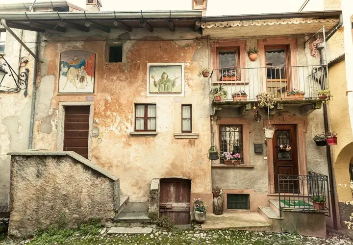 Antica facciata con affreschi e balcone fiorito. Un invito a scoprire cosa vedere ad Arcumeggia, tra arte e storia.