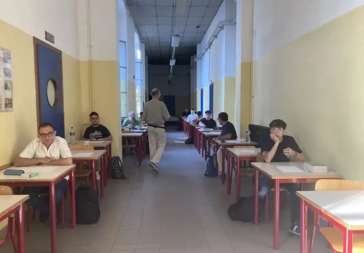 Studenti seduti ai banchi in un'aula scolastica, concentrati sull'esame di quinta elementare. Un insegnante cammina tra i banchi.