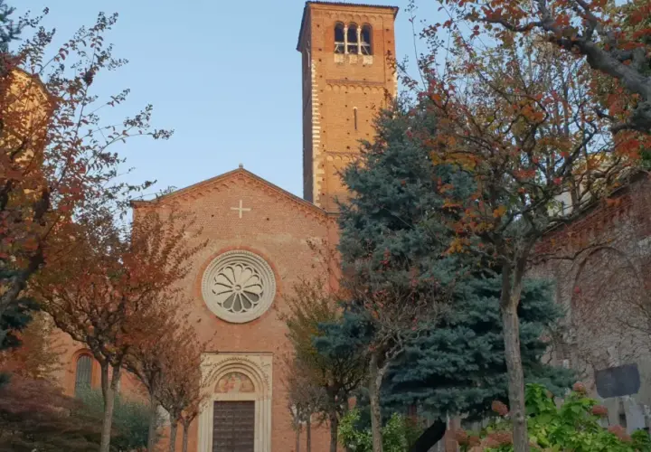 San Celso a Milano, con il suo campanile in mattoni rossi e la facciata ornata da un rosone, circondato da alberi dalle foglie autunnali.
