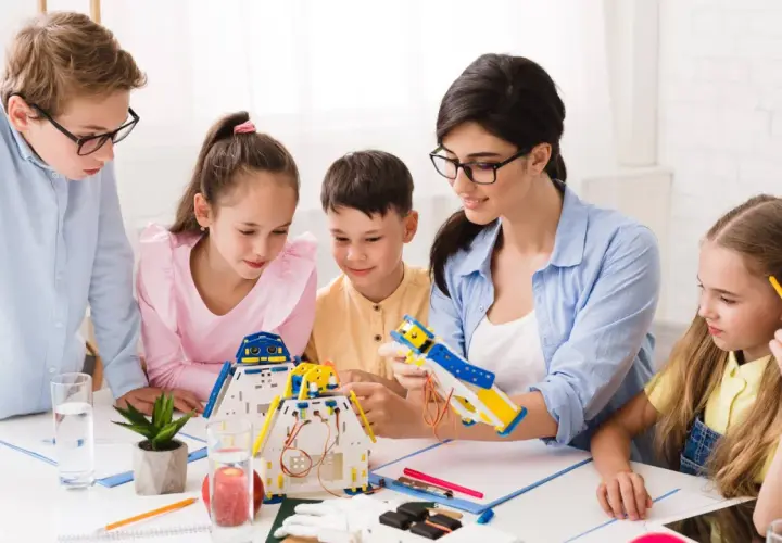 Bambini e insegnante costruiscono robot, un'attività che illustra il significato di itp scuola: apprendimento pratico e innovazione.
