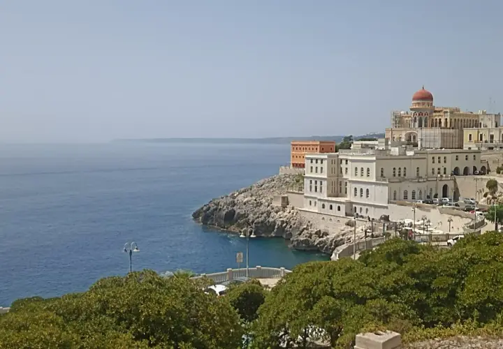 Vista sul mare e sul complesso dell'istituto alberghiero Santa Cesarea Terme, con edifici bianchi e una cupola rossa.
