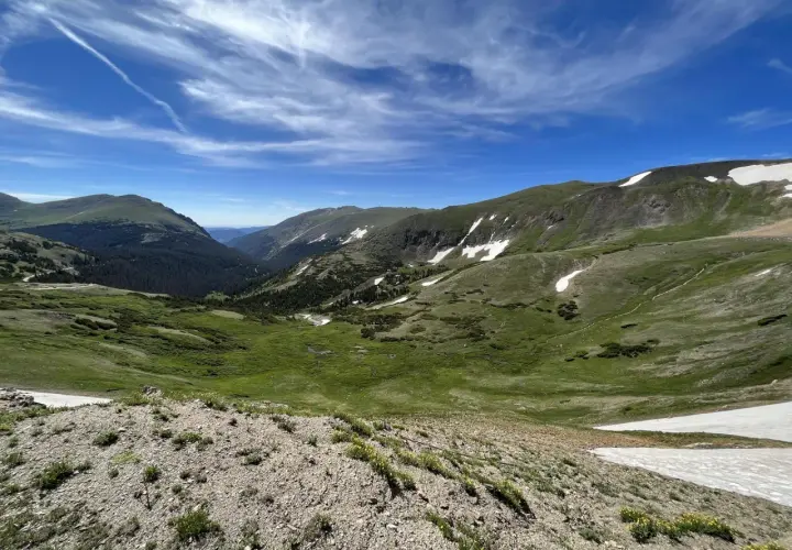 Vasta valle alpina con prati verdi, macchie di neve e cielo azzurro. Un paesaggio mozzafiato che ricorda l'altitudine chiusa di Bolzano.