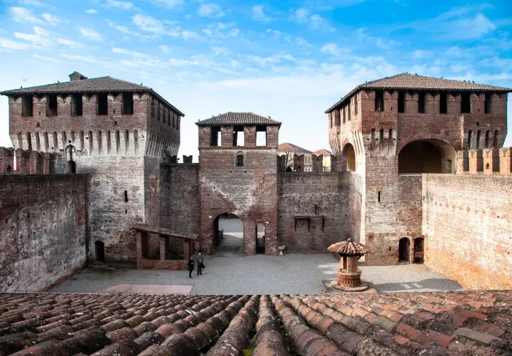 Il castello di Soncino, con le sue imponenti torri in mattoni rossi e le mura merlate, si staglia sotto un cielo azzurro e nuvoloso.