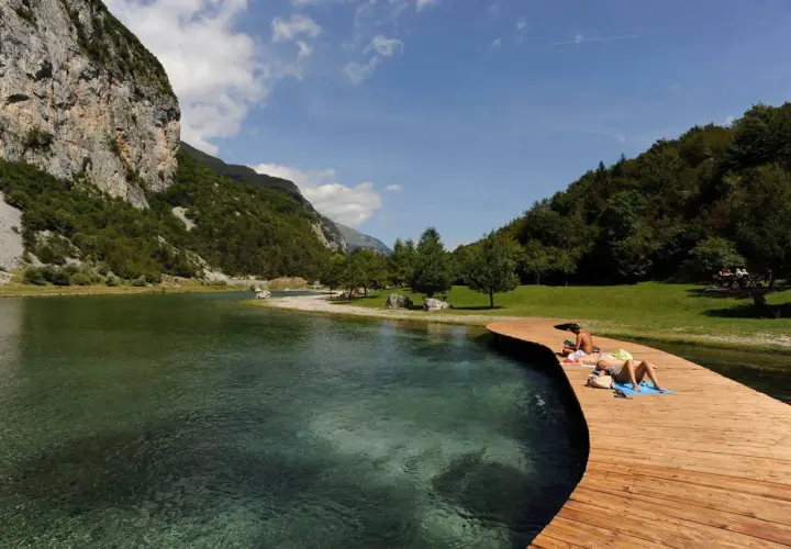 Persone si rilassano sul pontile in legno del lago di Nembia, circondato da montagne verdi e acqua cristallina.