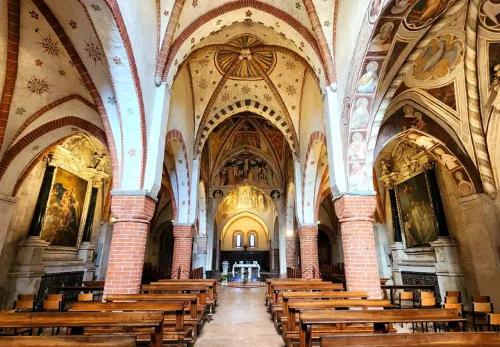 Interno dell'abbazia di Viboldone con volte affrescate, colonne in mattoni e panche di legno.