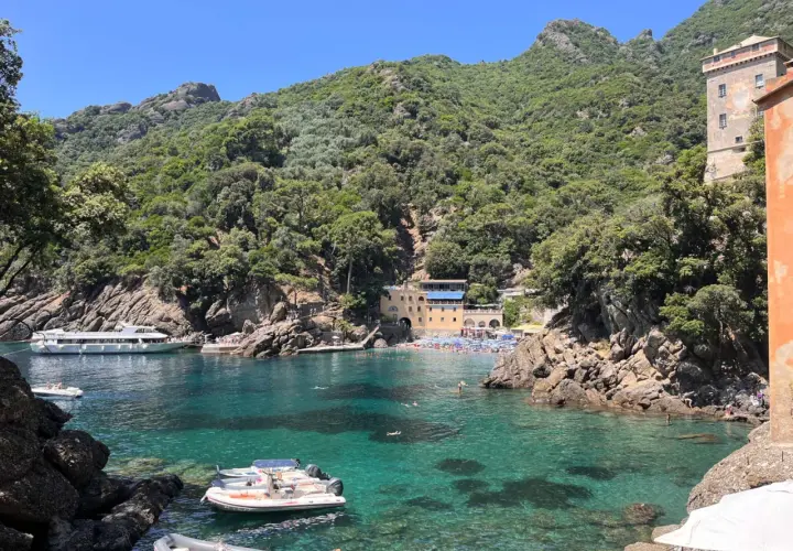 Baia di San Fruttuoso con acque cristalline, barche e persone che nuotano. Un luogo ideale per il trekking e il relax.
