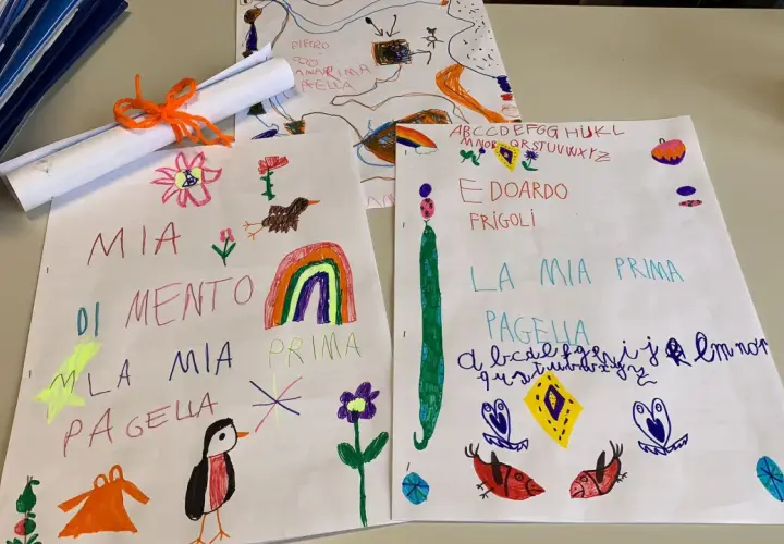 Disegni e scritte a mano, tra cui "Mia Pagella" e l'alfabeto, mostrano i voti elementari di bambini.